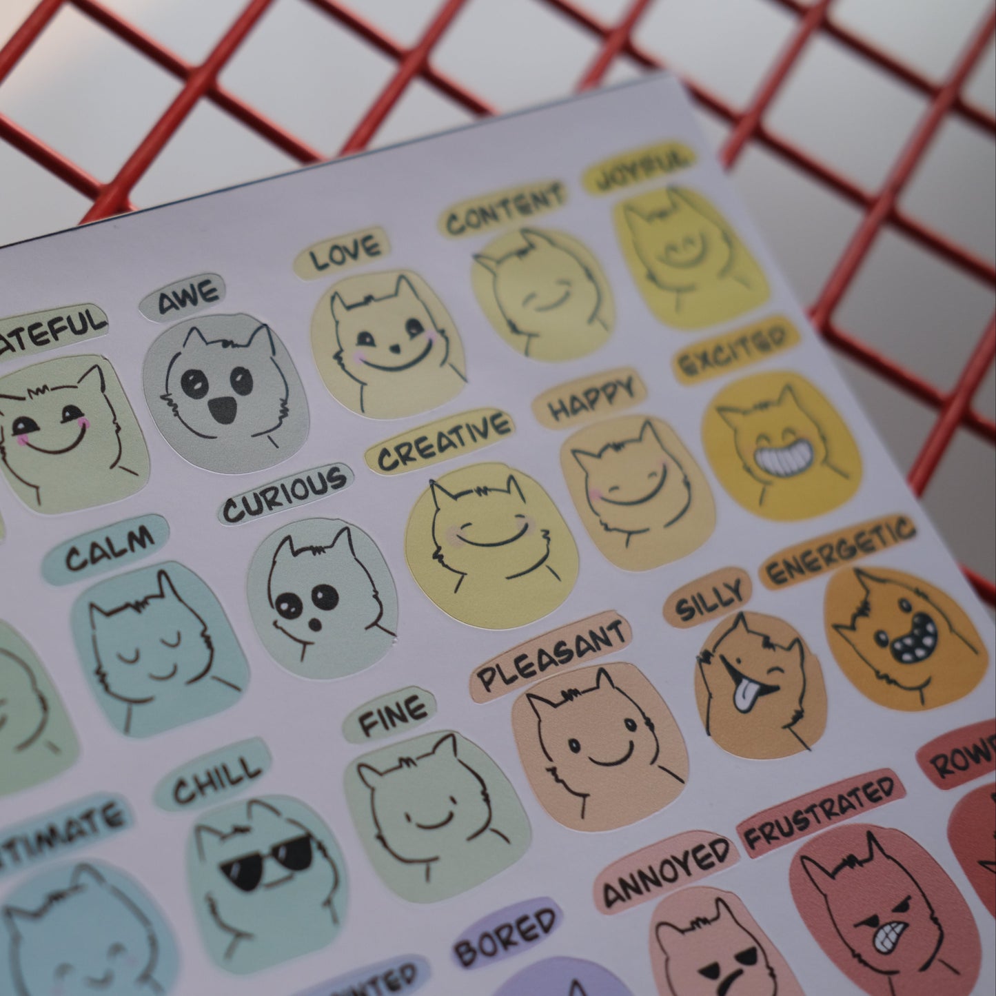 Sheet of cat-themed stickers with various expressions on a red grid background