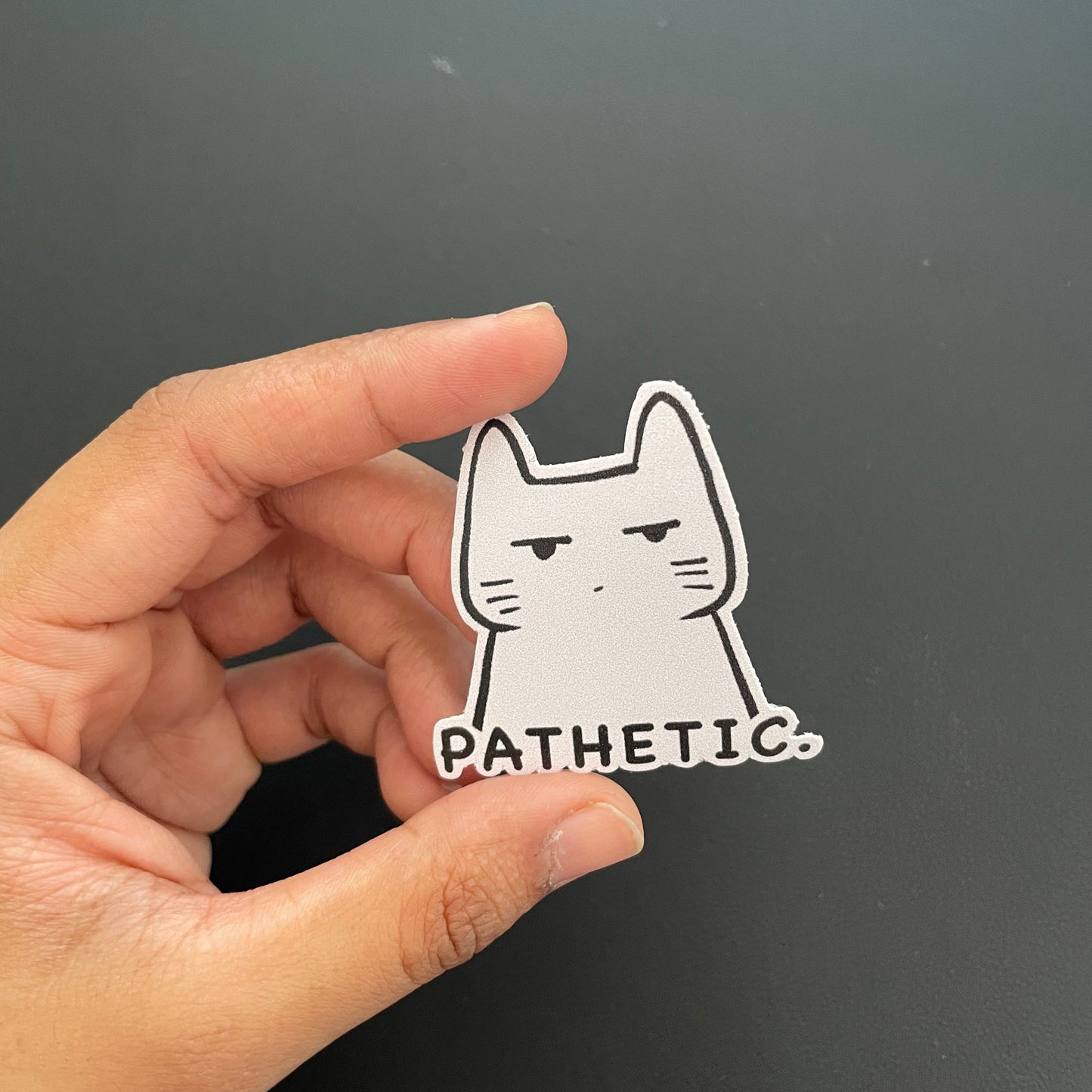 Hand holding a white cat sticker against a black background