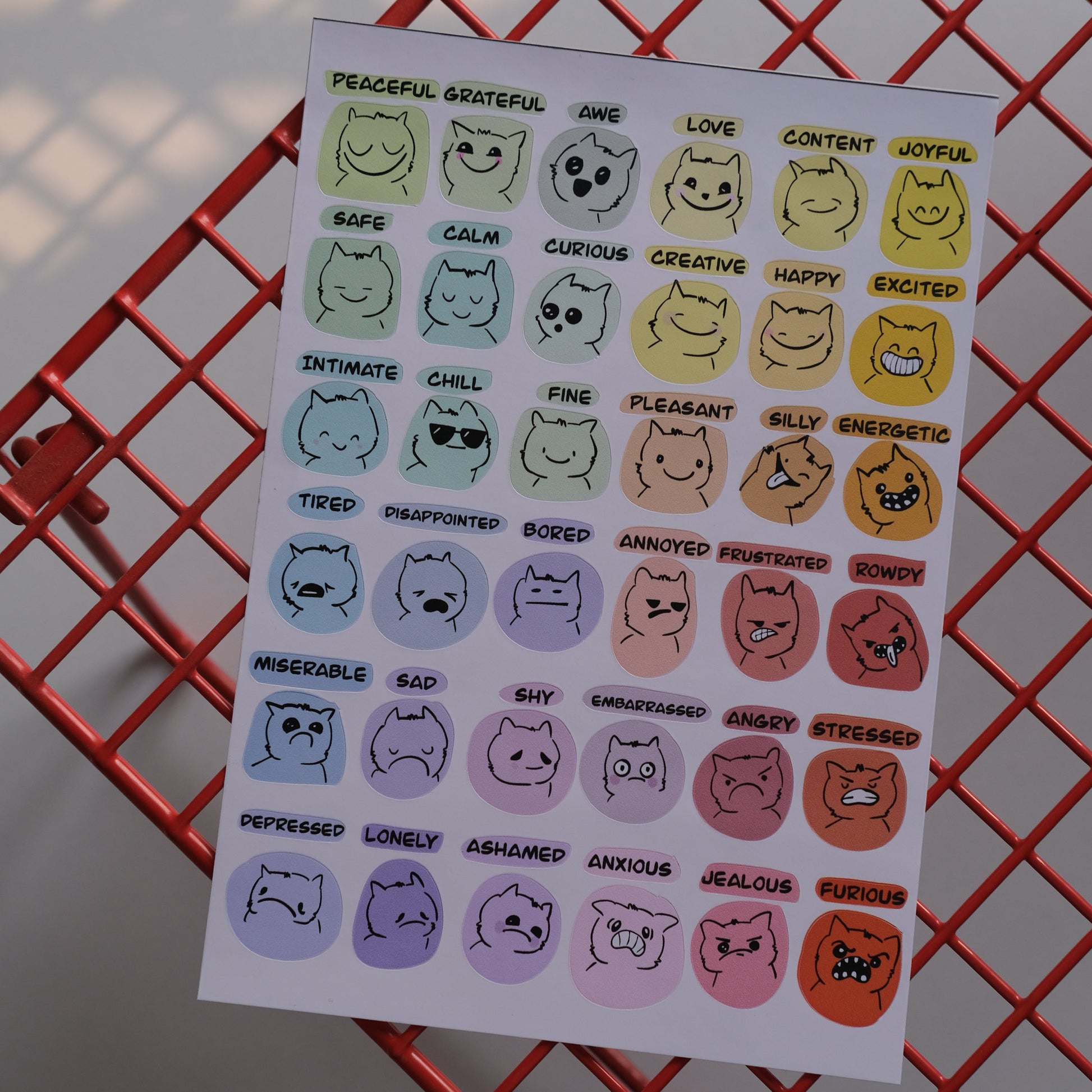 Sheet of colorful cat face stickers on a red wire basket.