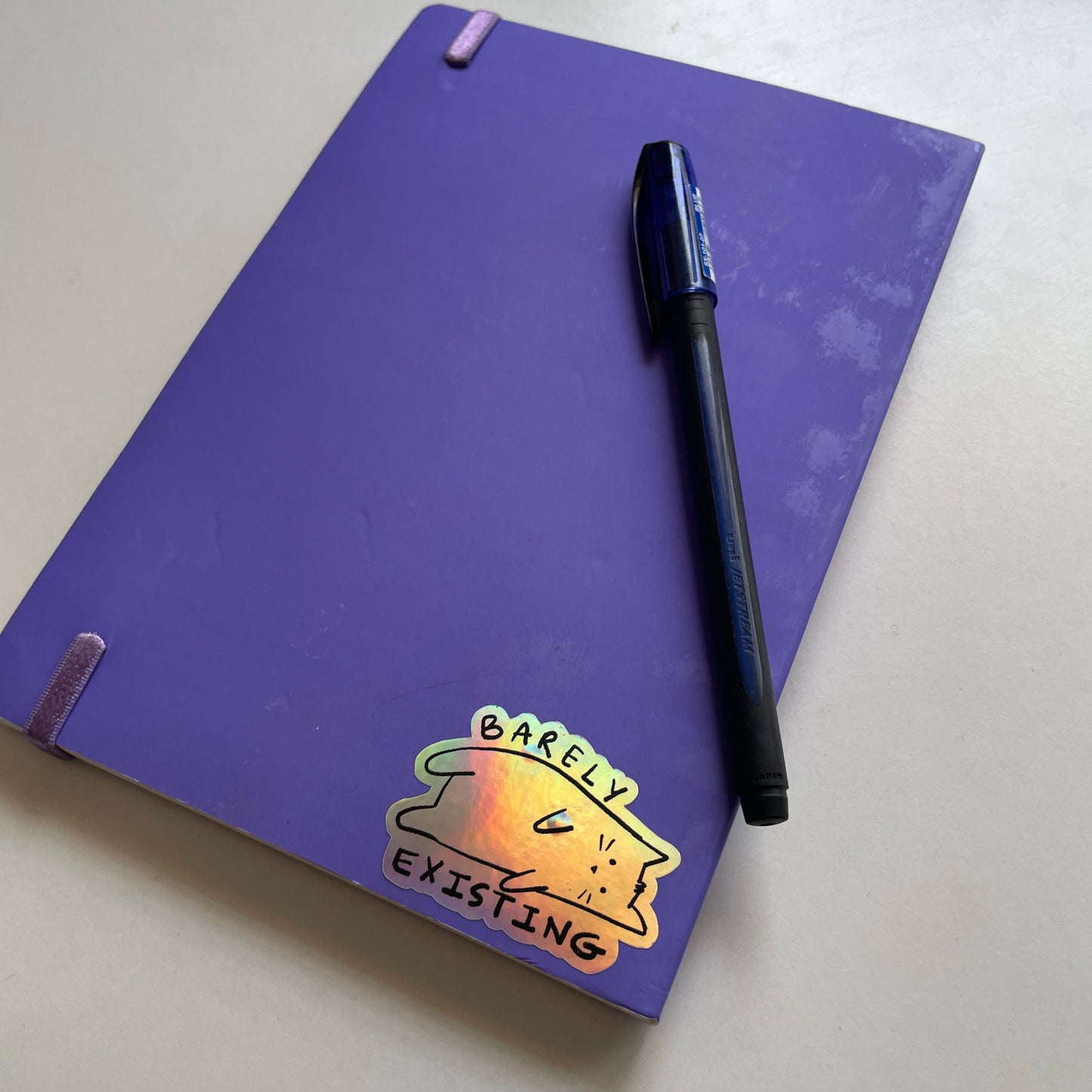 Purple notebook with a cat sticker and a pen on a light gray surface