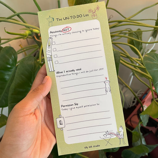 Green notepad with a to-do list titled 'The UN-TO-DO List' against a plant background.